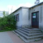 Zdjęcie przedstawia fragment starego budynku szkoły, w którym znajdują się drzwi wejściowe. Mają kolor brązowy, są częściowo przeszklone. Prowadzą do nich 5-cio stopniowe schody.